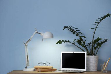 Laptop, kitaplar ve karanlık odada mavi duvarın yanında parlayan masa lambasıyla rahat çalışma alanı