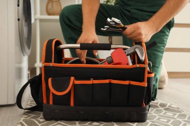 Banyoda çamaşır makinesini tamir eden bir çanta dolusu aleti olan erkek tesisatçı.