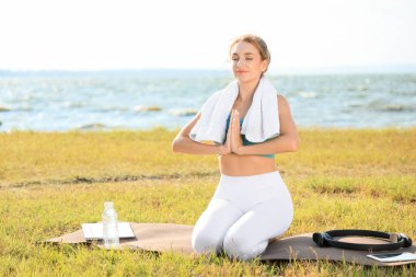 Havluyla parkta meditasyon yapan genç bir bayan.