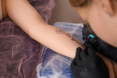 Güzellik salonunda kadının koluna dövme yapan sanatçı, yakın plan.