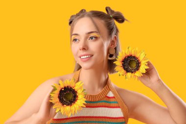 Şık makyajlı ve sarı arka planda ayçiçekleri olan güzel, genç ve mutlu bir kadın.