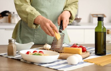 Mutfaktaki masada peyniri rendeleyen kadın, yakın plan.