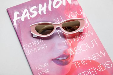 Gri arkaplanda şık güneş gözlüğü ve dergi