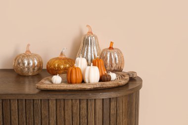 Balkabağı şeklinde mumlar ve bej duvarın yanında cam balkabakları olan çekmeceler.