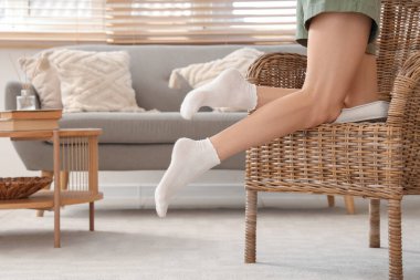 Beyaz çoraplı bir kadın evinde koltukta oturuyor.