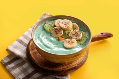 Lezzetli spirulina smoothie, ahşap tepsi ve sarı arka planda peçete, yakın plan