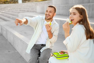Öğle yemeği molasında dışarıda bir şeye işaret eden sandviçleri olan genç bir çift.
