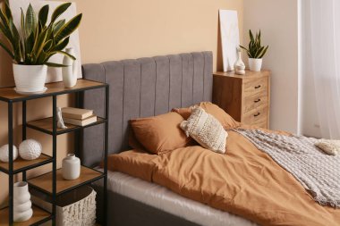 Yatak odasının içinde yastıklı, raf üniteli ve çekmeceli büyük rahat bir yatak.