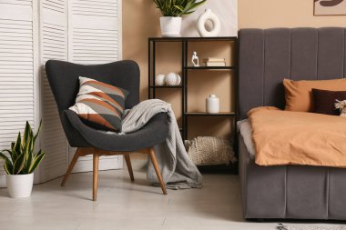 Şık yatak odasının içinde yastıklı ve ekoseli rahat bir koltuk.