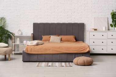 Yastıklı rahat bir yatak, raf ünitesi, çekmeceler ve şık bir yatak odasının içindeki puf.