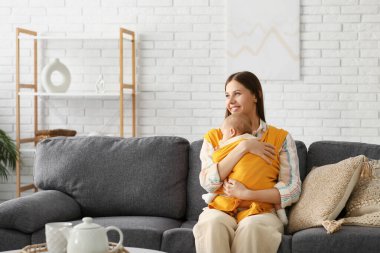 Oturma odasındaki kanepede oturan küçük bebeği olan genç bir anne.