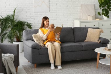 Evde kitap okuyan küçük bir bebeği olan mutlu bir anne.