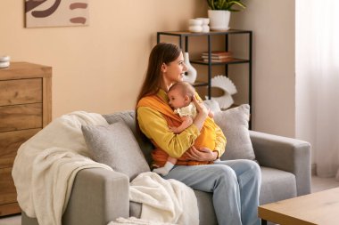 Evde kanepede oturan küçük bir bebeği olan mutlu genç bir anne.