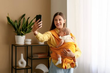 Küçük bir bebeği olan genç bir anne oturma odasında selfie çekiyor.