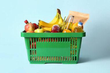 Farklı taze ürünlerle dolu yeşil alışveriş sepeti ve mavi arka planda muzlar.
