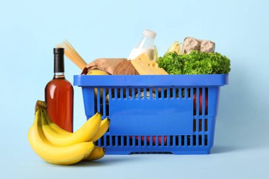 Bir şişe şarap, muz, mavi alışveriş sepeti farklı taze ürünler ve mavi arka planda bir şişe süt.