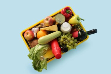 Farklı taze ürünlerle dolu sarı alışveriş sepeti ve mavi arka planda bir şişe şarap. Üst görünüm