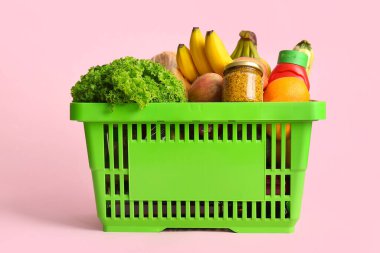 Farklı taze ürünlerle dolu yeşil alışveriş sepeti ve pembe arka planda hardal.