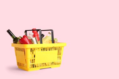 Farklı taze ürünlerle dolu sarı alışveriş sepeti ve pembe arka planda dolma biber.