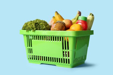 Farklı taze ürünlerle dolu yeşil alışveriş sepeti ve mavi arka planda hardal.