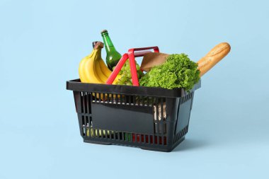 Farklı taze ürünlerle dolu siyah alışveriş sepeti ve mavi arka planda baget.