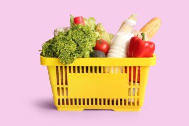 Farklı taze ürünlerle dolu sarı alışveriş sepeti ve leylak arka planda bir şişe süt.