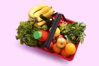 Farklı taze ürünlerle dolu kırmızı alışveriş sepeti ve leylak arka planda muzlar. Üst görünüm