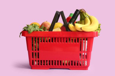 Farklı taze ürünlerle dolu kırmızı alışveriş sepeti ve leylak arka planda muzlar