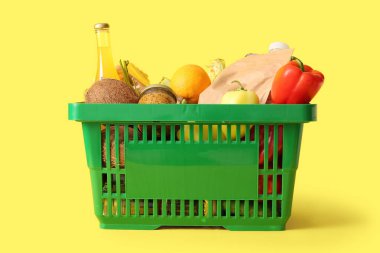 Farklı taze ürünlerle dolu yeşil alışveriş sepeti ve sarı arka planda dolma biber.