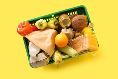 Farklı taze ürünlerle dolu yeşil alışveriş sepeti ve sarı arka planda dolma biber. Üst görünüm