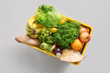 Beyaz arka planda farklı taze ürünler ve elmalarla dolu sarı alışveriş sepeti. Üst görünüm