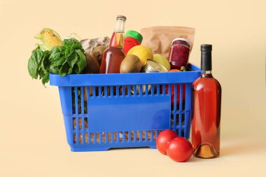 Bir şişe şarap, domates, farklı taze ürünlerle dolu mavi alışveriş sepeti ve bej arka planda ıspanak.