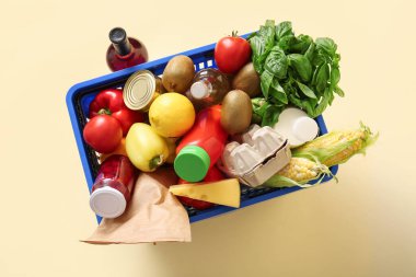 Bir şişe şarap, farklı taze ürünlerle dolu mavi alışveriş sepeti ve bej arka planda ıspanak. Üst görünüm