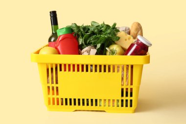 Farklı taze ürünlerle dolu sarı alışveriş sepeti ve bej arka planda ketçap.