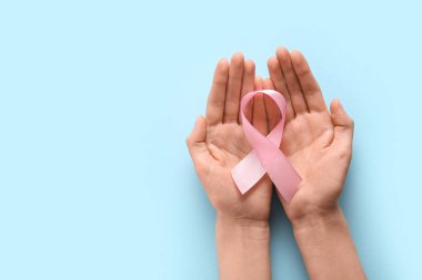 Mavi arka planda pembe kurdeleli kadın eller. Dünya Kanser Günü