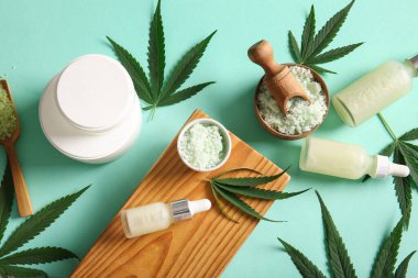 Turkuaz arka planda kenevir kozmetik yağı, deniz tuzu, yaprak ve krema kavanozları