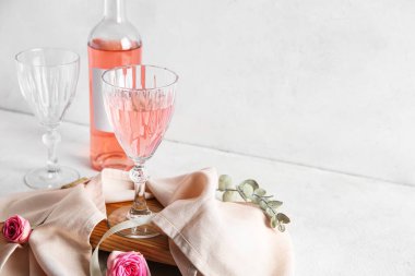 Cam, bir şişe pembe şarap ve beyaz arka planda güllerle bez.