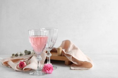 Bir bardak pembe şarap, bez ve beyaz arka planda güllerle dolu boş bir bardak.