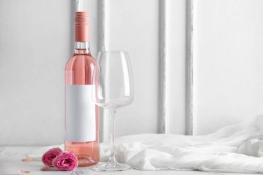Bir şişe pembe şarap, bez ve beyaz arka planda güllerle dolu boş bardaklar.
