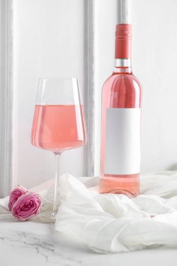 Cam, bir şişe pembe şarap ve beyaz arka planda güllerle bez.