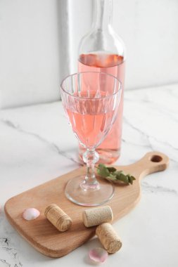 Güvertede bir bardak pembe şarap ve beyaz arka planda mantarlar.