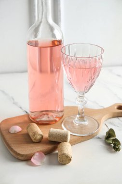 Bir şişe ve bir bardak pembe şarap ve beyaz arka planda duran mantarlar.