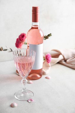 Beyaz arka planda güllerle dolu cam ve bir şişe pembe şarap.