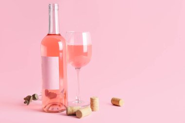 Bir şişe pembe şarap ve okaliptüs dalı ve pembe arka planda mantarlar.