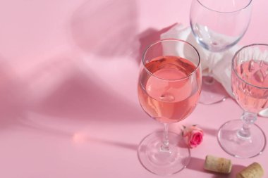 Şarap kadehleri, pembe arka planda gül ve bez.