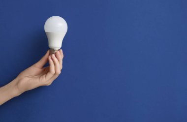 Koyu mavi arka planda beyaz ampullü kadın eli