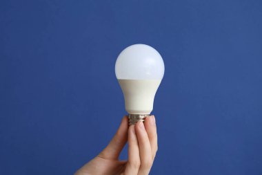 Koyu mavi arka planda beyaz ampullü kadın eli