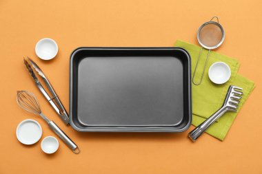 Pişirme tepsisi, peçete, çırpı, maşa, kevgir ve kase bej arka planda. Üst görünüm