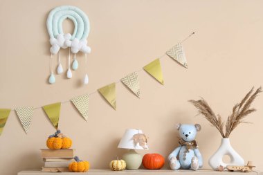 Kitapları, lambası ve oyuncak ayısı olan balkabakları çocuk odasındaki bej duvarın yanında rafta.