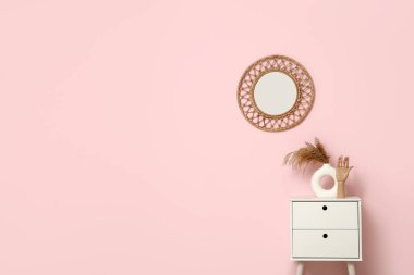 Komodinin yanında vazoda otlar ve odada pembe duvarda aynalar var.